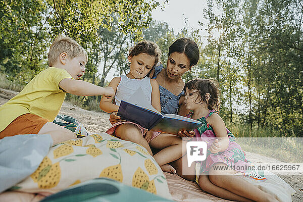 Ältere Frau und drei Kinder lesen ein Buch am Strand
