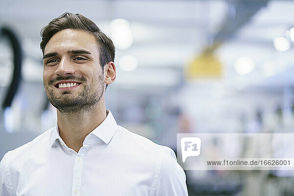 Smiling young male professional looking away while standing at illuminated factory