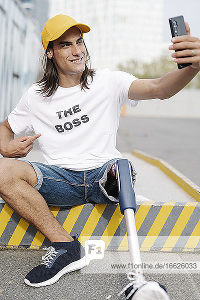 Mann mit Bein- und Fußprothese macht Selfie  während er auf der Straße in der Stadt sitzt
