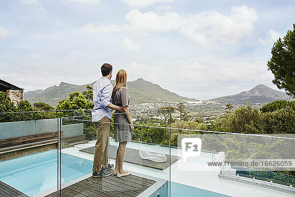 Heterosexuelles Paar steht und betrachtet die Aussicht vom Balkon eines modernen Hauses
