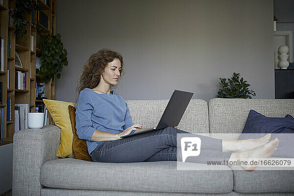 Frau arbeitet am Laptop  während sie zu Hause auf dem Sofa sitzt