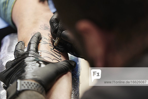 Close-up of male artist tattooing on customer's hand in studio
