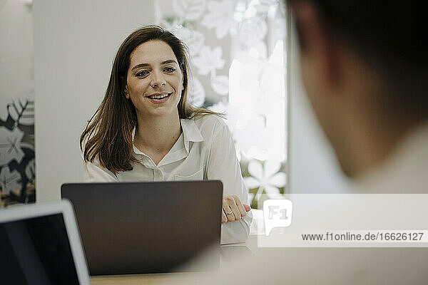 Geschäftsfrau mit Laptop im Gespräch mit Partner im Büro