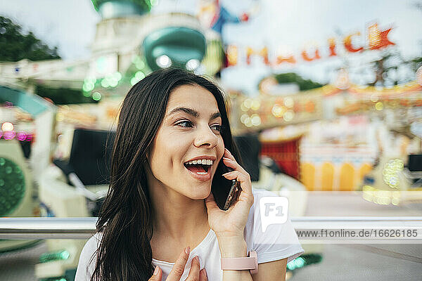 Close-up of cheerful woman talking over smart phone at amusement park