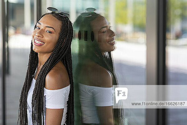 Young woman smiling while leaning on glass wall in city
