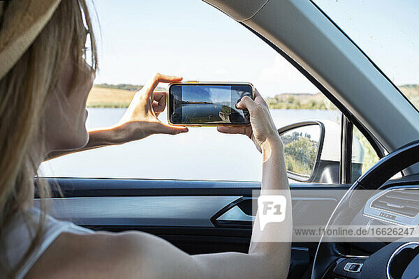 Junge Frau  die im Auto sitzend mit dem Handy fotografiert