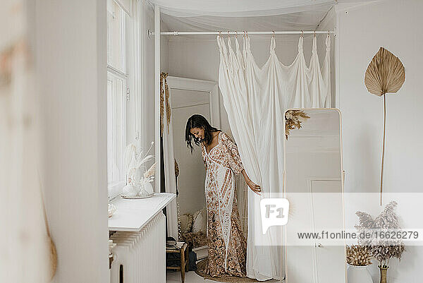 Young bride trying on wedding dress while standing at home