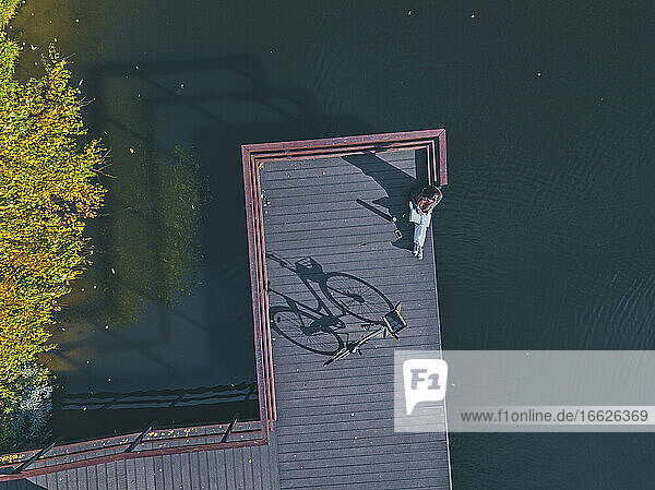 Aerial view of young woman reading book at edge of coastal jetty