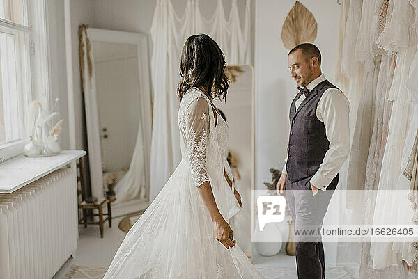 Junge Braut schaut in den Spiegel  während der Bräutigam mit den Händen in der Tasche zu Hause steht