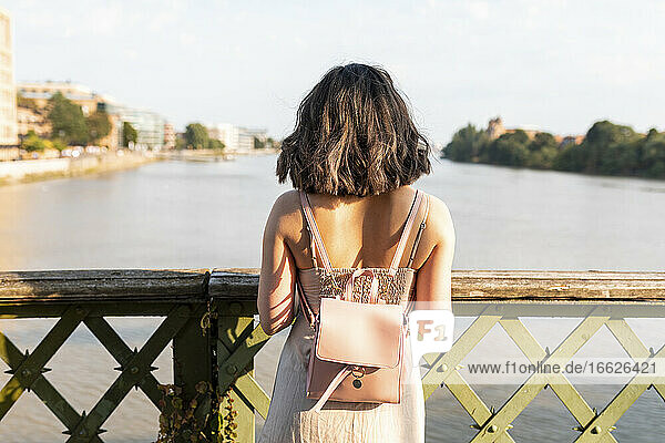 Frau steht an einem sonnigen Tag auf einer Fußgängerbrücke und schaut auf den Fluss