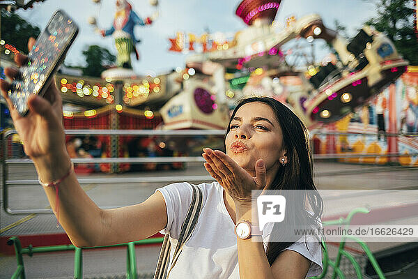 Young woman blowing kiss while taking selfie at amusement park