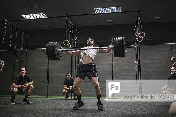 People cheering man lifting barbell while standing in gym