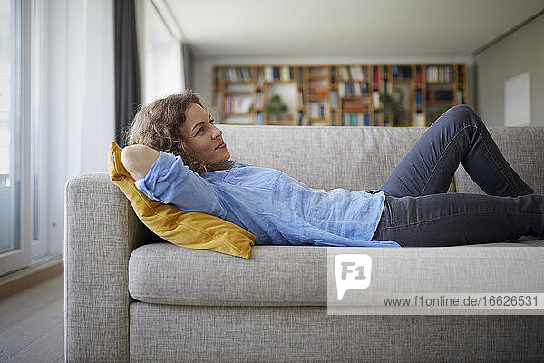 Frau mit Händen hinter dem Kopf auf dem Sofa liegend zu Hause