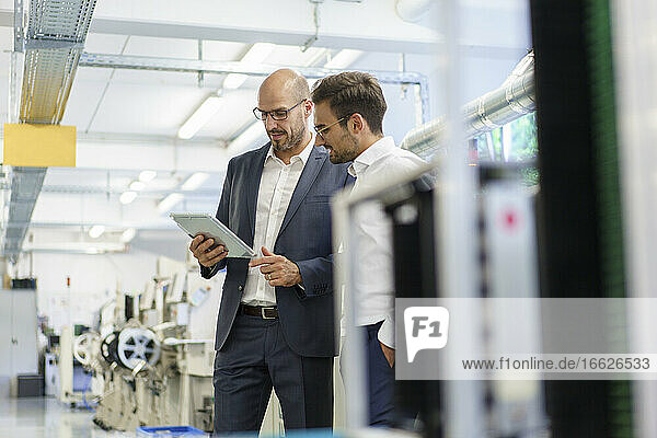 Businessmen discussing over digital tablet while standing at factory
