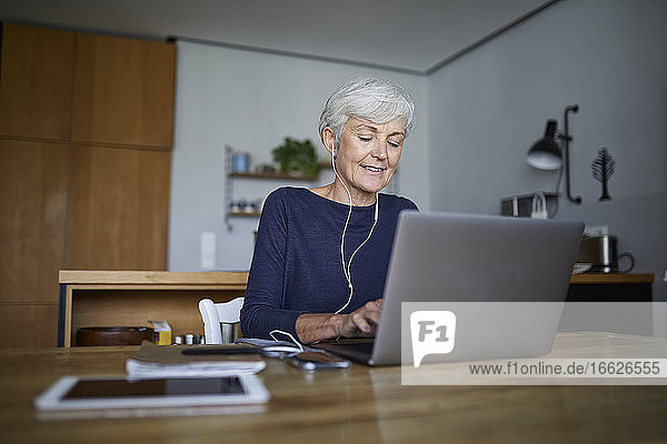 Aktiver Senior  der zu Hause sitzend am Laptop arbeitet und Musik hört