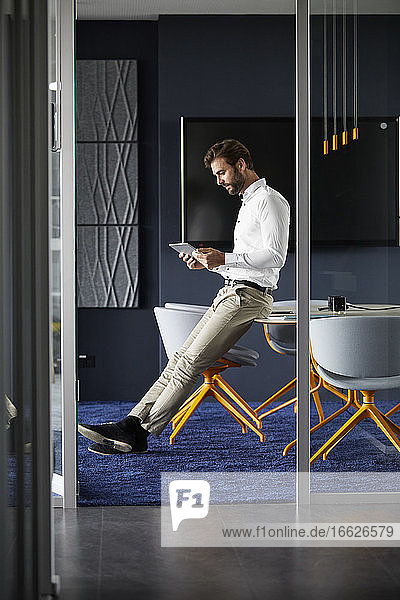 Geschäftsmann  der ein digitales Tablet benutzt  während er auf einem Tisch im Büro sitzt