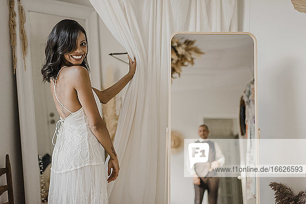 Reflexion des Bräutigams im Spiegel  während die Braut zu Hause über die Schulter schaut