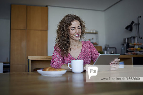 Frau mit Essen und Kaffee  die ein digitales Tablet benutzt  während sie zu Hause sitzt
