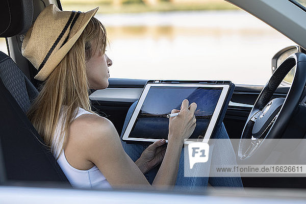 Frau  die im Auto sitzend mit einem digitalen Tablet malt