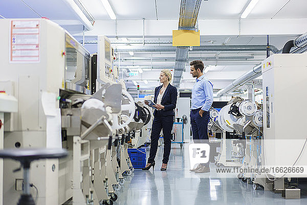 Männlicher Techniker steht neben einer Geschäftsfrau  die in einer Fabrik Maschinen analysiert