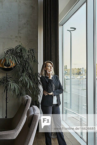 Thoughtful woman looking through window while standing in hotel lobby