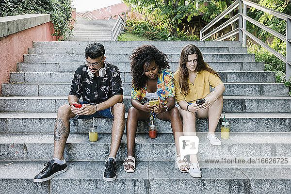 Junge Freunde schreiben SMS auf dem Smartphone  während sie auf den Stufen im Park sitzen