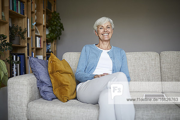 Lächelnde ältere Frau sitzt zu Hause auf dem Sofa