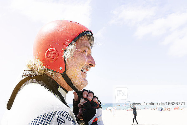 Close-up of smiling senior man wearing sports helmet at beach against sky during summer