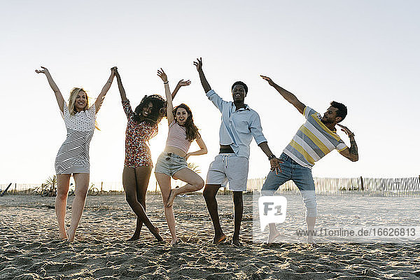 Cheerful friends doing hand gestures while standing on beach during sunny day