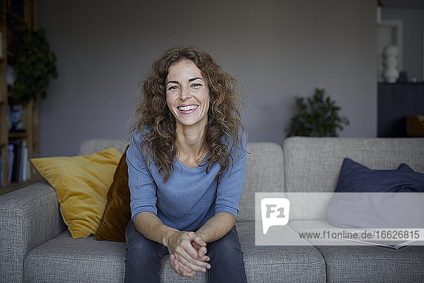 Schöne Frau lächelt  während sie zu Hause auf dem Sofa sitzt