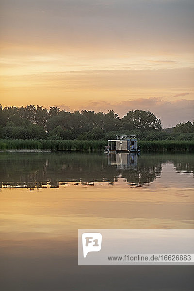 Reflektierendes Bild eines Hausbootes im See bei Sonnenuntergang
