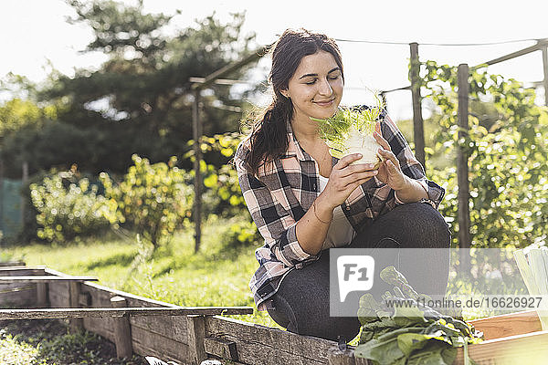 Smiling young woman with eyes closed smelling vegetable while crouching in garden