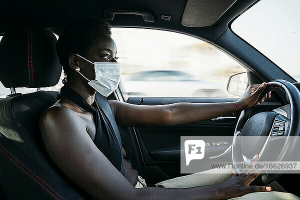 Junge Frau mit Gesichtsmaske  die sich auf das Autofahren konzentriert