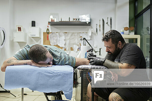 Male artist tattooing on customer's hand in studio
