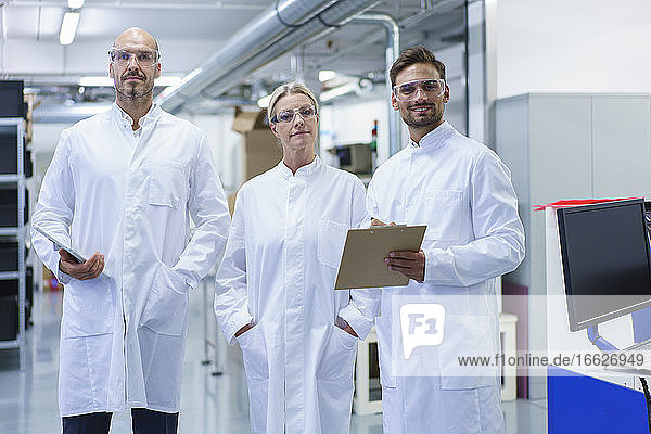 Selbstbewusste männliche und weibliche Wissenschaftler in weißen Laborkitteln stehen in einem beleuchteten Labor