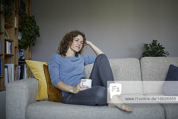 Thoughtful woman with head in hands sitting on sofa at home