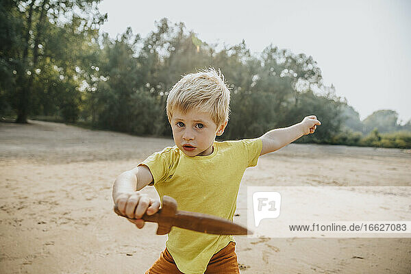 Niedlicher kleiner Junge spielt mit Holzdolch am Strand