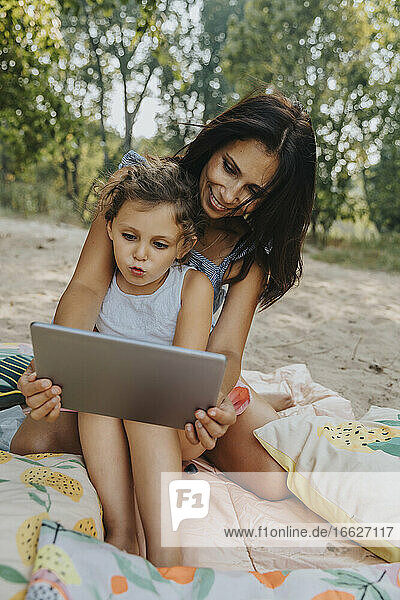 Mutter und Tochter benutzen digitales Tablet am Strand