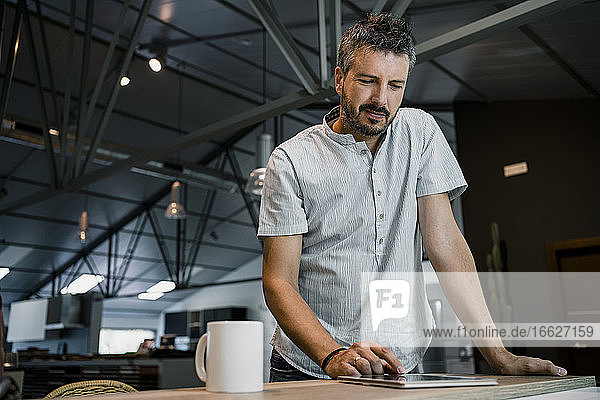 Gutaussehender reifer männlicher Freiberufler  der im Büro stehend ein digitales Tablet benutzt