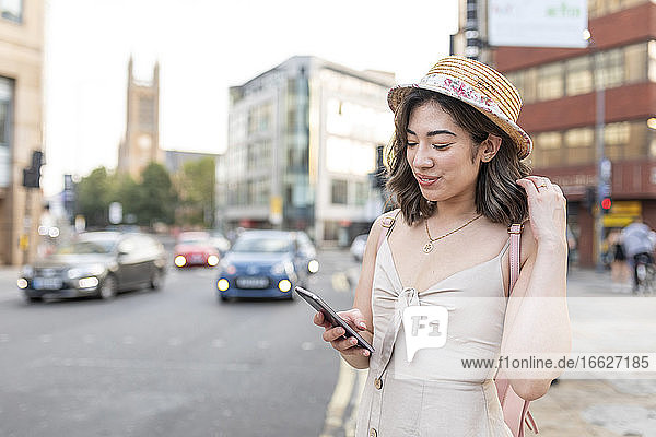 Frau lächelt  während sie eine Textnachricht auf einem Smartphone in der Stadt schreibt