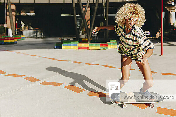 Confident blond woman skateboarding on footpath during sunny day