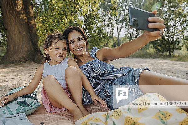 Mutter und Tochter machen ein Selfie mit dem Smartphone am Strand