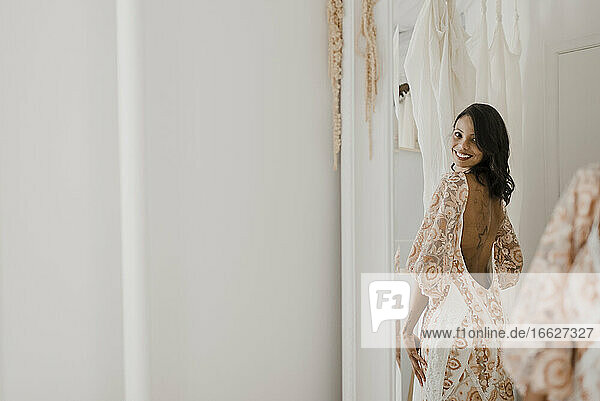 Lächelnde junge Braut schaut über die Schulter in den Spiegel zu Hause
