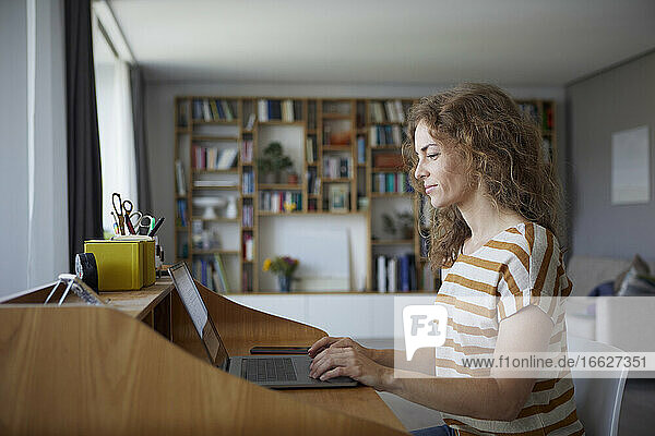 Frau arbeitet am Laptop  während sie zu Hause am Schreibtisch sitzt
