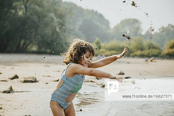 Cute girl throwing sand and mud while standing at beach