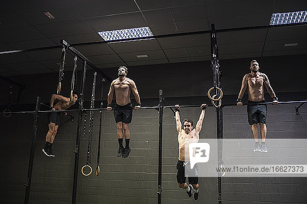 Athletes doing pull ups exercise on rod at gym