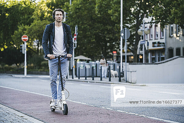 Mann hört Musik  während er in der Stadt mit einem elektrischen Roller fährt