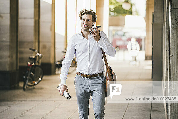 Smiling man talking on phone while walking at building in city