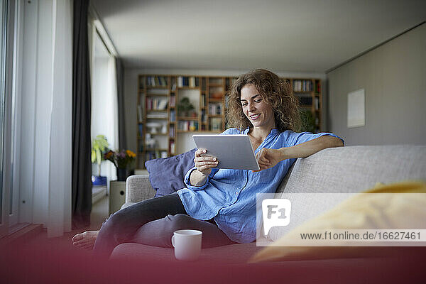 Frau benutzt digitales Tablet  während sie zu Hause auf dem Sofa sitzt