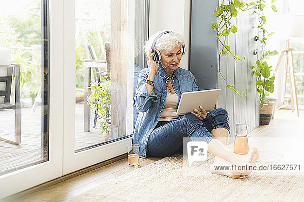 Mature woman listening to music while working on digital tablet